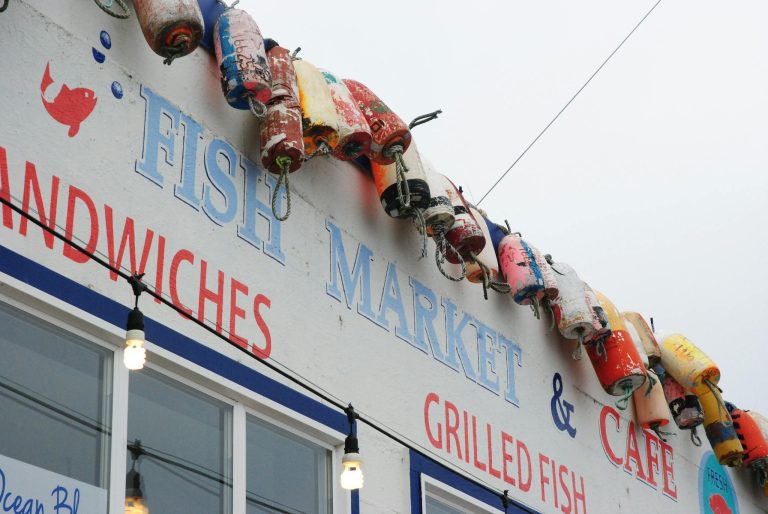 Colorful buoys decorate a fish market and café sign, inviting visitors to enjoy fresh seafood.