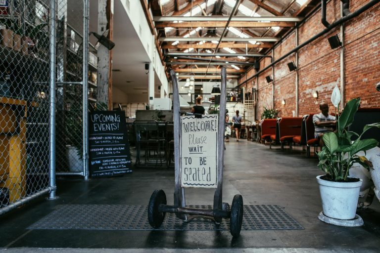 Industrial-style restaurant interior with seating sign and vibrant plants.